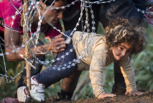 A refugee girl moves under barbed wire as she crosses from Serbia to Hungary, in Roszke, Thursday, Aug. 27, 2015. Over 10,000 migrants, including many women with babies and small children, have crossed into Serbia over the past few days and headed toward Hungary. (AP Photo/Darko Bandic)