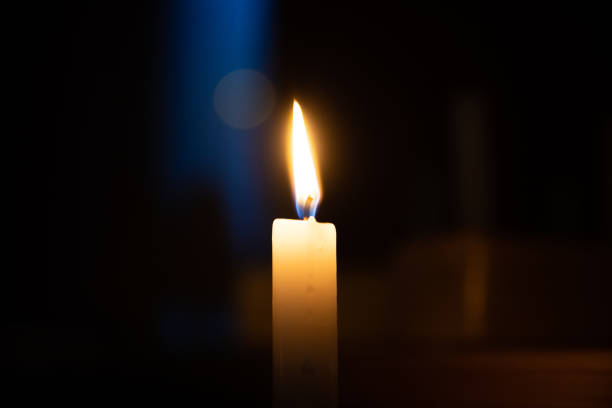 Yellow candle is burning on a dark background. Blue stripe of light, hot fire. A symbol of sorrow, mourning, loss, rest in peace